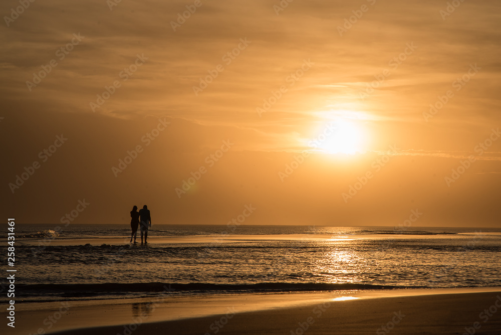 Couple walking on the beach at sunset, reflection of the sun on the sea, sunset orange Couple walking on the beach at sunset, reflection of the sun on the sea, sunset orange