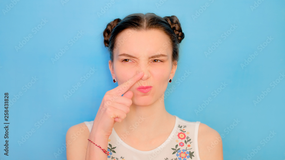 Funny cute girl on a blue studio background. Bright emotional female portrait. Woman wrinkles nose from bad smell Funny cute girl on a blue studio background. Bright emotional female portrait. Woman wrinkles nose from bad smell