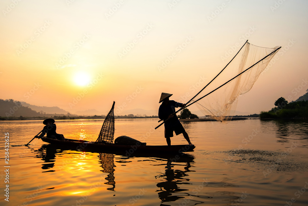 Asia fisherman net using on wooden boat casting net sunset or sunrise in the Mekong river - Silhouette fisherman