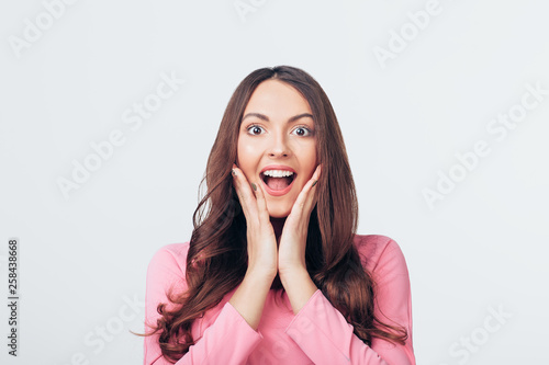 Young happy and surprised woman looking to camera and holds cheeks by hands isolated on white backround