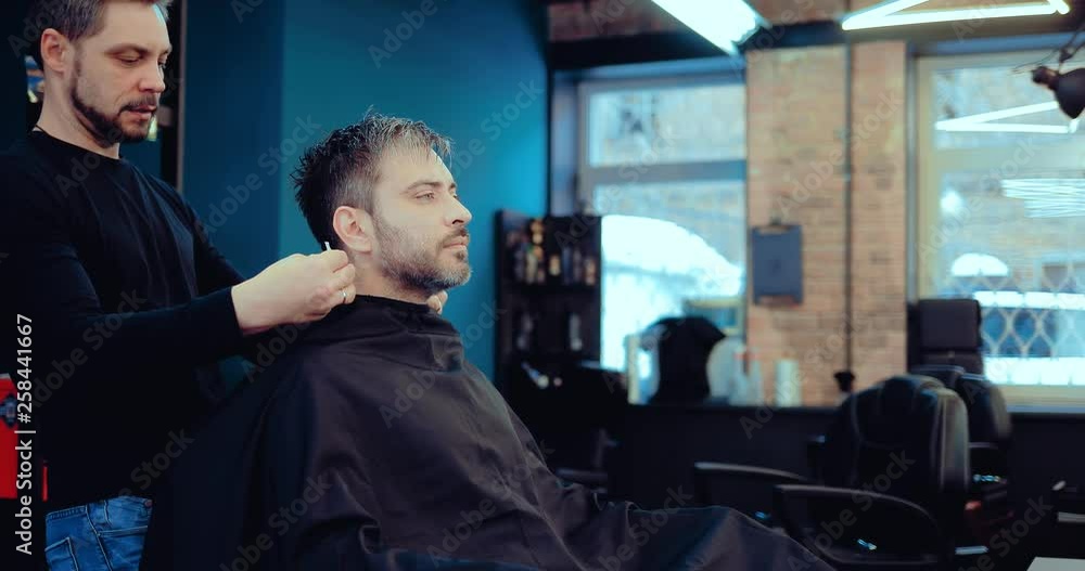 Brutal male barber is putting a paper collar around his neck. Stylist touches the client's hair, tries on the hairstyle. Stylish men's hair salon. Brutal male barber is putting a paper collar around his neck. Stylist touches the client's hair, tries on the hairstyle. Stylish men's hair salon.