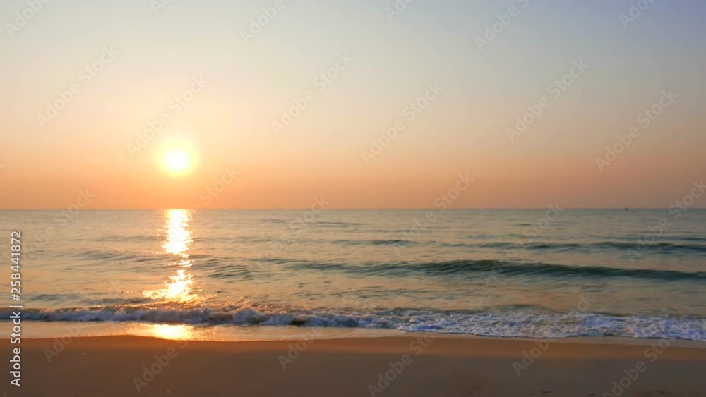 A huge golden sun hangs in an orange sky just above the horizon as the waves below roll to the beach below. A huge golden sun hangs in an orange sky just above the horizon as the waves below roll to the beach below.