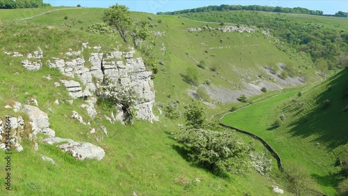 Panorama of the Lathkill Dale in the Peak District, England, with a solitary man sitting on the edge of a high limestone rock and watching the scenic landscape of the valley. photo