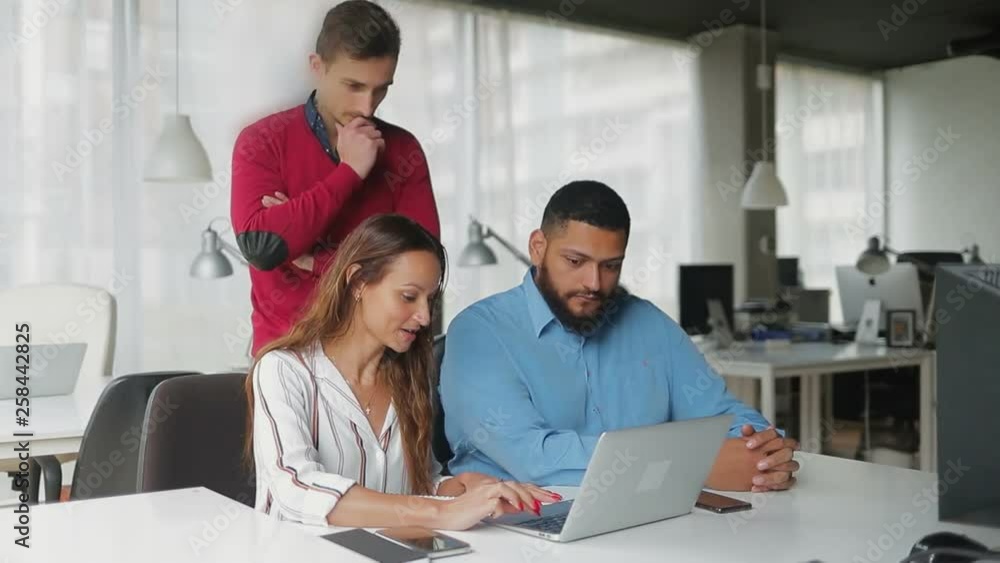 Cheerful business team working with laptop in modern office. Smiling young managers using laptop in office. Business and technology concept Cheerful business team working with laptop in modern office. Smiling young managers using laptop in office. Business and technology concept
