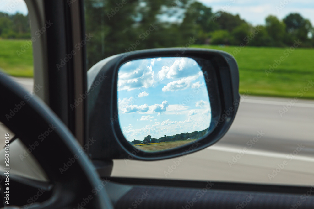 Reflection of blue sky with clouds in the mirror of a riding car in sunny day on the road.  