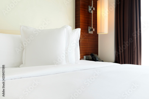 White pillows on bed covered with white sheets by the window