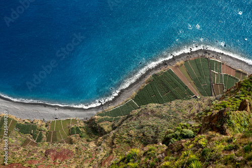 Top view of the coast of the island of Madeira with a coastline and areas with planted plants. Cropped shot, top view, free space for text, horizontal. Nature and agriculture concept.
