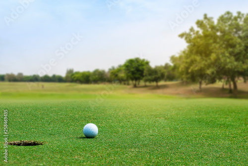White Golf ball on green course near hole on blurred landscape of golf course in bright day time with copy space. Sport, Recreation, Relax in holiday concept 