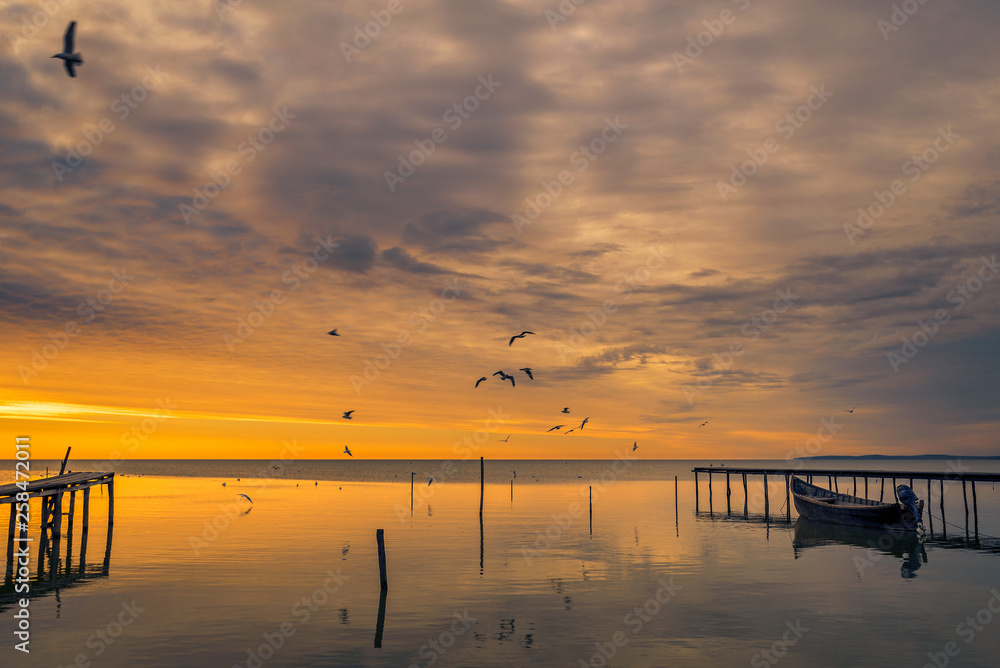 Lake scene in the morning at sunrise with birds flying above the lake and a boat near a pontoon