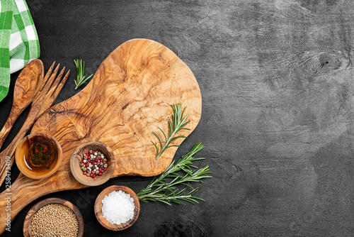 Cutting Board, rosemary and spices on a black wooden table.