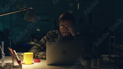 Attractive effective office worker working hard at his cabinet late at night, drinks tea and programming something on his computer. Workaholic, freelance position, making money. He is sitting in his