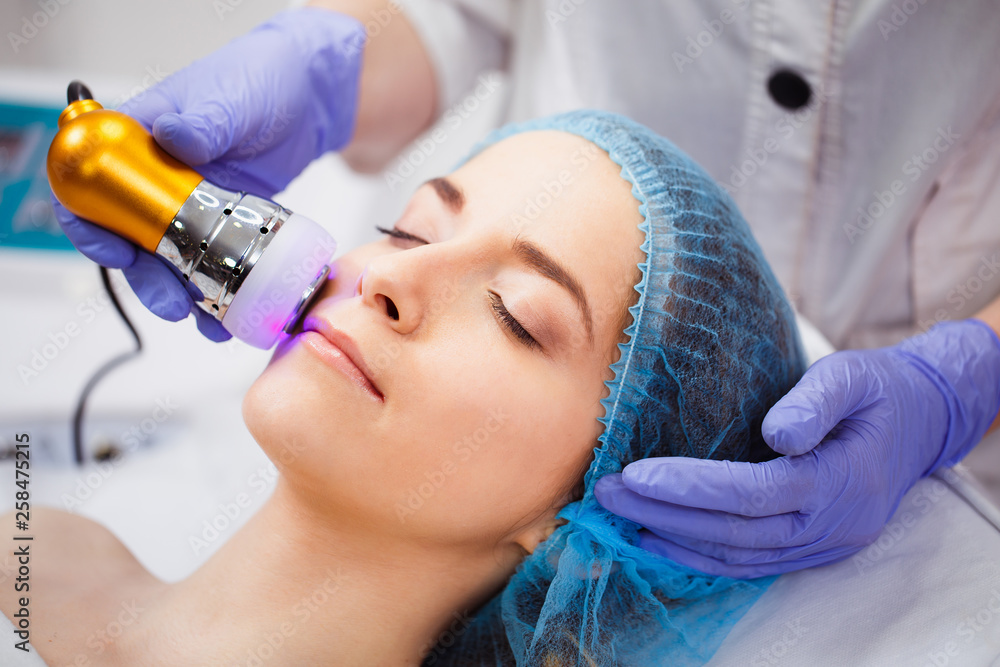 Obraz premium The procedure of photoepilation in the beauty salon. A young woman is removed unwanted hair on her face. Hardware cosmetology. Microcurrent therapy. Close up