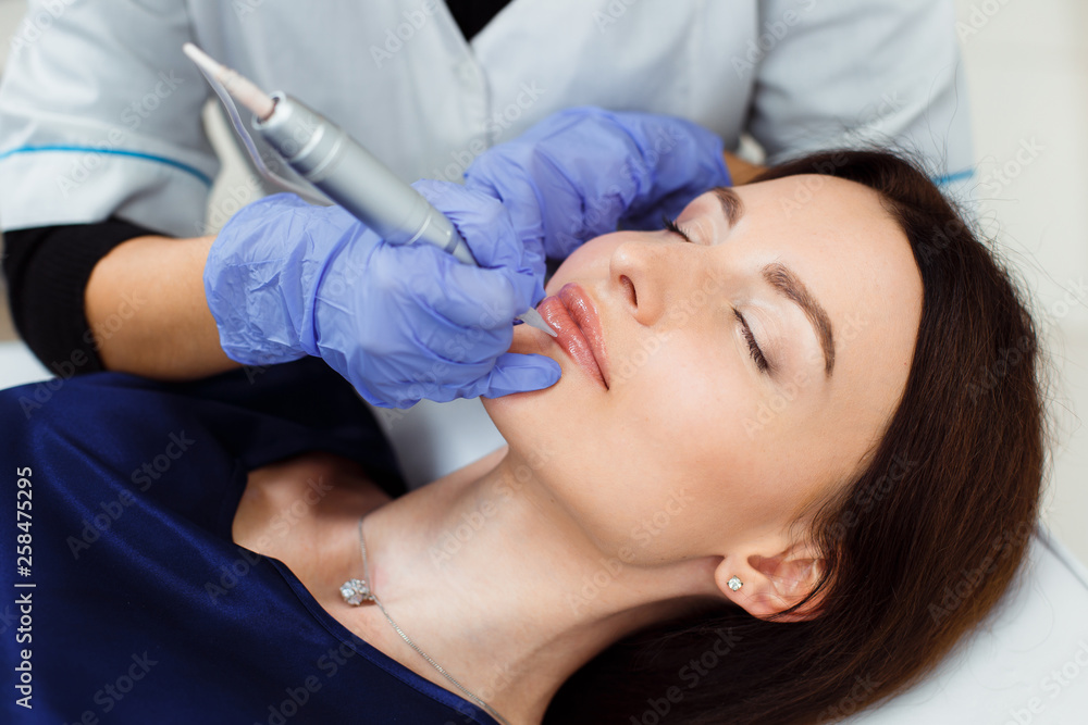 Young woman having permanent makeup on lips in beautician salon. Close up Young woman having permanent makeup on lips in beautician salon. Close up