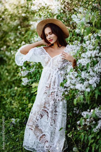 young woman in a straw hat in lilac. Model in white pennuar among flowers