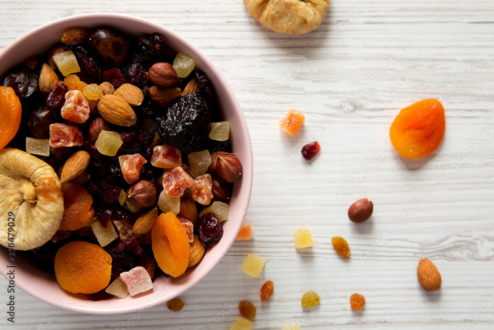 Dried fruits and nut mix in a pink bowl on a white wooden table, top view. Overhead, from above, flat lay. Close-up. Dried fruits and nut mix in a pink bowl on a white wooden table, top view. Overhead, from above, flat lay. Close-up.
