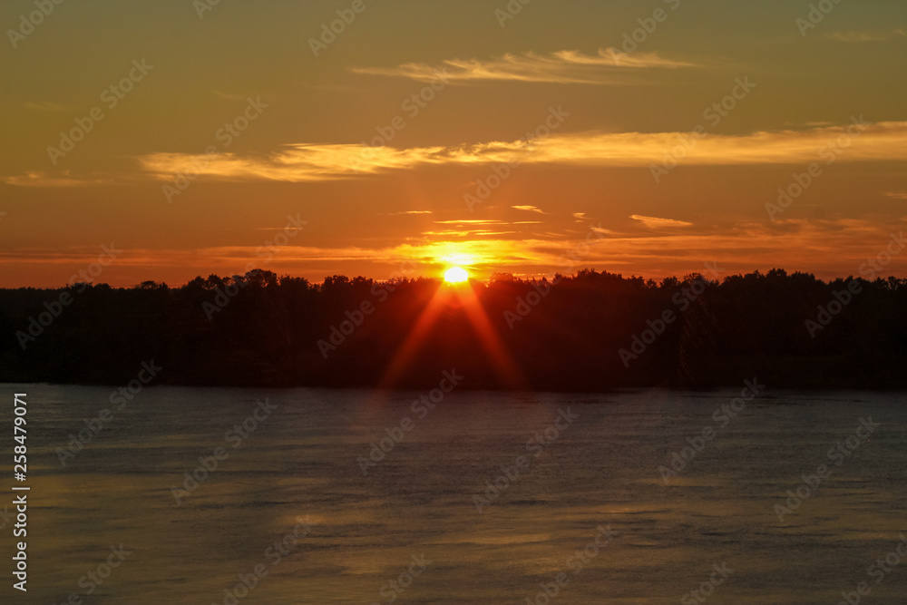 Beautiful deep morning dawn with highlights in the orange rays of the summer sun on a river Volga with sun glare.. Toned in orange colour and backlit. Beautiful deep morning dawn with highlights in the orange rays of the summer sun on a river Volga with sun glare.. Toned in orange colour and backlit.