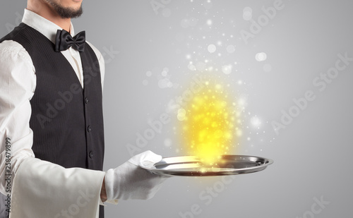 Elegant young waiter serving mysterious light on tray 