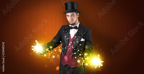 Handsome illusionist holding his superpower on his hands with gold wallpaper