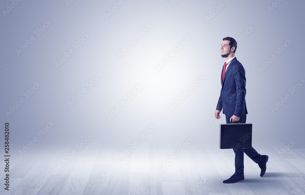 Successful businessman walking in front of an empty wall with briefcase on his hand
Successful businessman walking in front of an empty wall with briefcase on his hand
