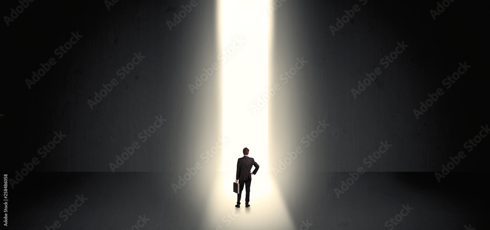 Businessman standing and seeing the light at the end of a big wall
