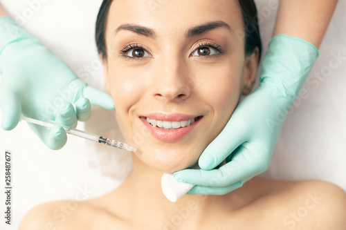 Top view of emotional woman smiling and beautician holding syringe
