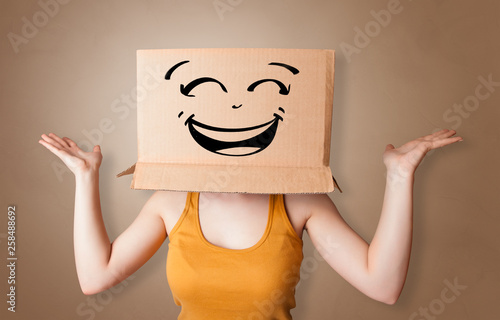 Young woman with happy face illustrated cardboard box on her head 