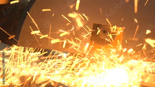Disc grinder cutting a rectangular metallic tube with flying yellow sparkles