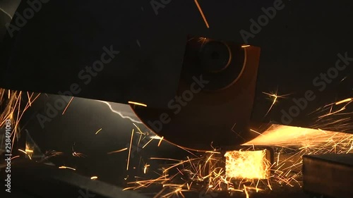 Angle grinder cutting a rectangular metallic pipe with flying yellow sparkles