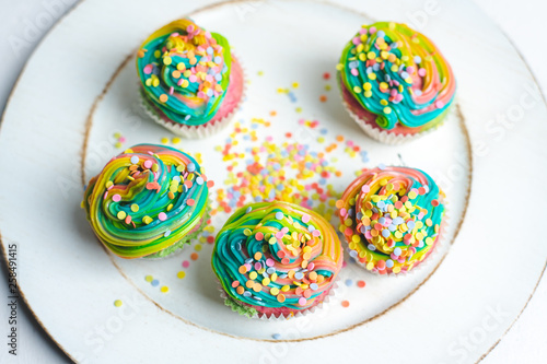 beautiful, bright, very colorful muffins decorated with rainbow cream and candy confetti, on a bright, spring background