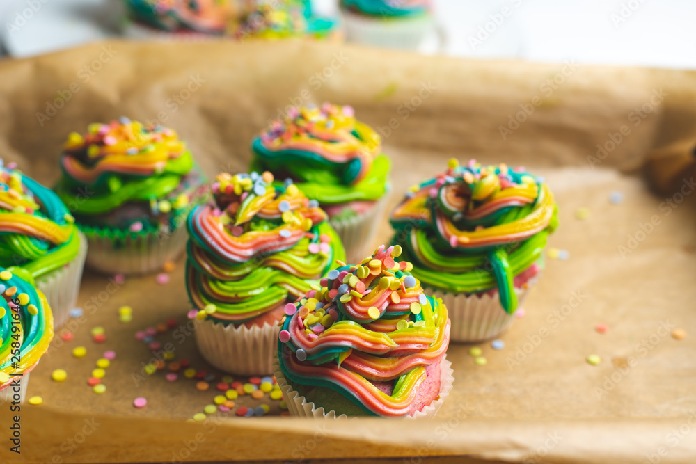beautiful, bright, very colorful muffins decorated with rainbow cream and candy confetti, on a bright, spring background