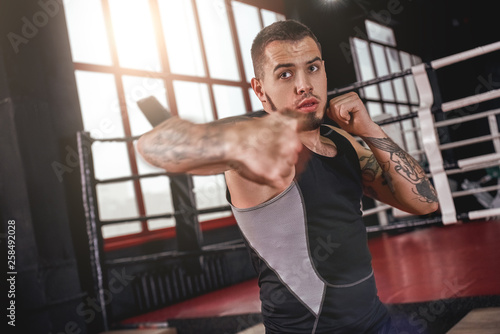 Great hook. Muscular athlete in sports clothing throwing hook punch opposite boxing ring
