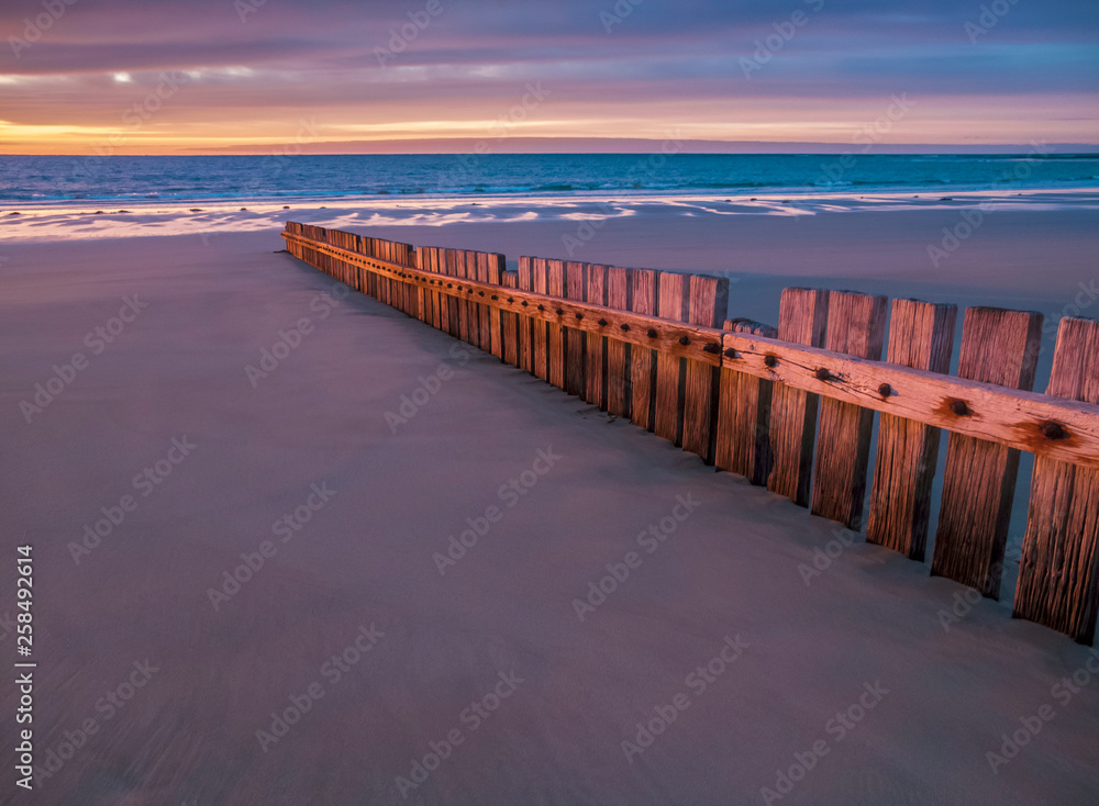 Wooden groin or fence on beach to control erosion and sand movement, dawn or dusk.