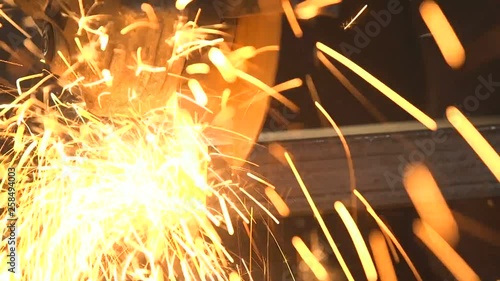 Man with angle grinder cutting a long metallic billet with plazma sparkles