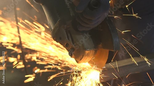 Side grinder cutting a rectangular metallic pipe with speedy yellow sparkles