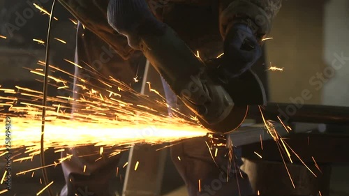 Man with side grinder cutting a long metallic bar with plazma sparkles