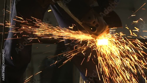 Guy with disc grinder cutting a long metallic billet with plazma sparkles