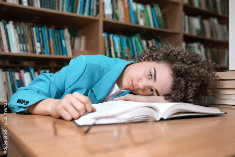 Young beautiful curly girl in glasses and blue suit sitting with books in the library. Student Study Young beautiful curly girl in glasses and blue suit sitting with books in the library. Student Study