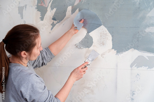 woman tears off Wallpaper, removing Wallpaper from the wall with a spatula, the process of updating the wall room repair. with free text space