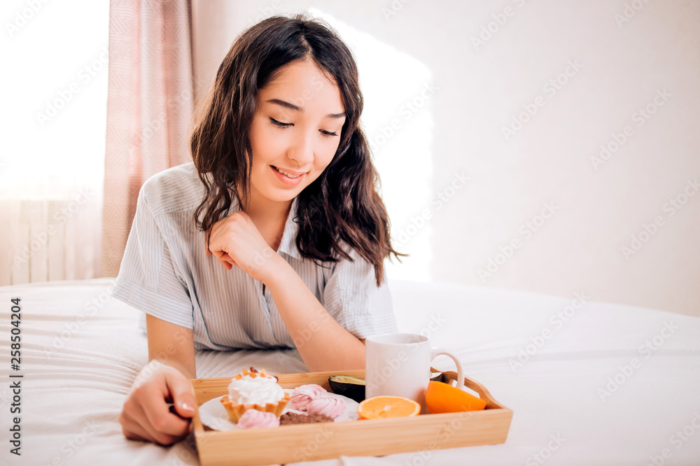 Tender beautiful caucasian girl in pajamas smiling looking away resting relaxing at home. Amazing joyful brunette woman enjoying morning on bed in hotel room. Relaxation, home comfort. Tender beautiful caucasian girl in pajamas smiling looking away resting relaxing at home. Amazing joyful brunette woman enjoying morning on bed in hotel room. Relaxation, home comfort.