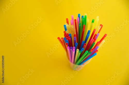 Multicolored plastic tubules for a cocktail in a glass on a yellow background. Polymers in everyday life.