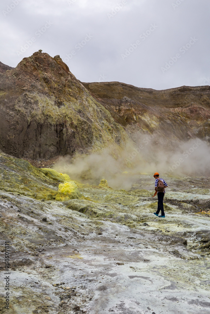 Portrait view of a hiker exploring the sulphur fumaroles and hot mud springs on edge of crater - White Island, New Zealand.
