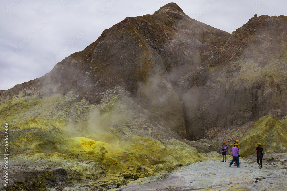 Tourists in hard hats and wearing gas masks stand by sulphur fumaroles and hot mud springs on edge of crater - White Island, an active volcano in the Bay of Plenty, New Zealand.