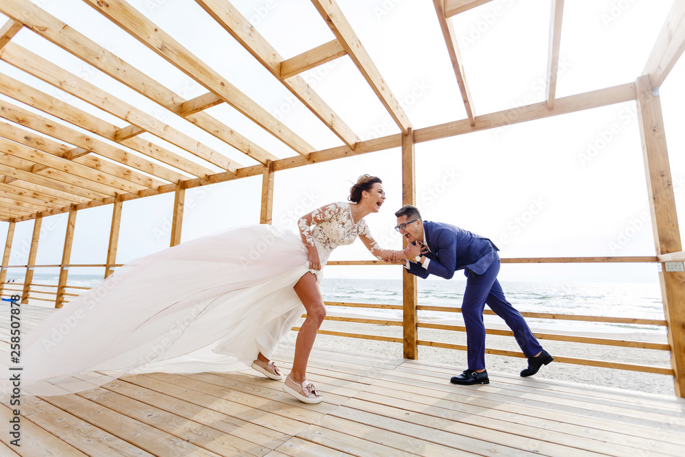 groom holds his bride tightly in a strong wind on the beach