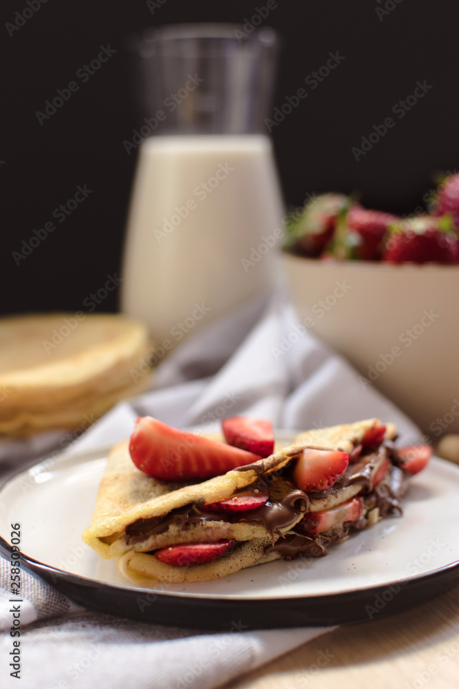 crepes with strawberries and chocolate cream, black background crepes with strawberries and chocolate cream, black background