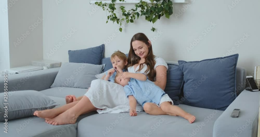 Mom hugs her two little sons on the couch in the living room and watches TV. Family watching TV Mom hugs her two little sons on the couch in the living room and watches TV. Family watching TV