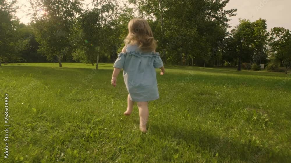 Baby girl running through the grass in garden in sunset sunlight. Slow motion. Happy smiling baby girl. Baby girl running through the grass in garden in sunset sunlight. Slow motion. Happy smiling baby girl.