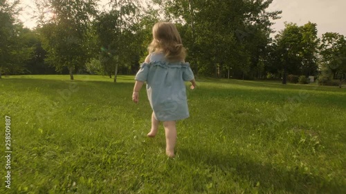Baby girl running through the grass in garden in sunset sunlight. Slow motion. Happy smiling baby girl.