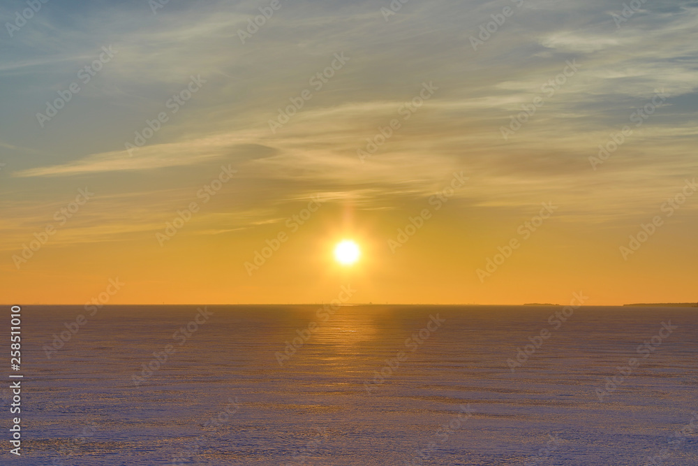 The sunset or sunrise. The cloudy sky cloured in red, orange, crimson, purple, violet and blue bright and vivid coloures with setting or rising sun over the sea, lake or bay covered with ice and snow The sunset or sunrise. The cloudy sky cloured in red, orange, crimson, purple, violet and blue bright and vivid coloures with setting or rising sun over the sea, lake or bay covered with ice and snow