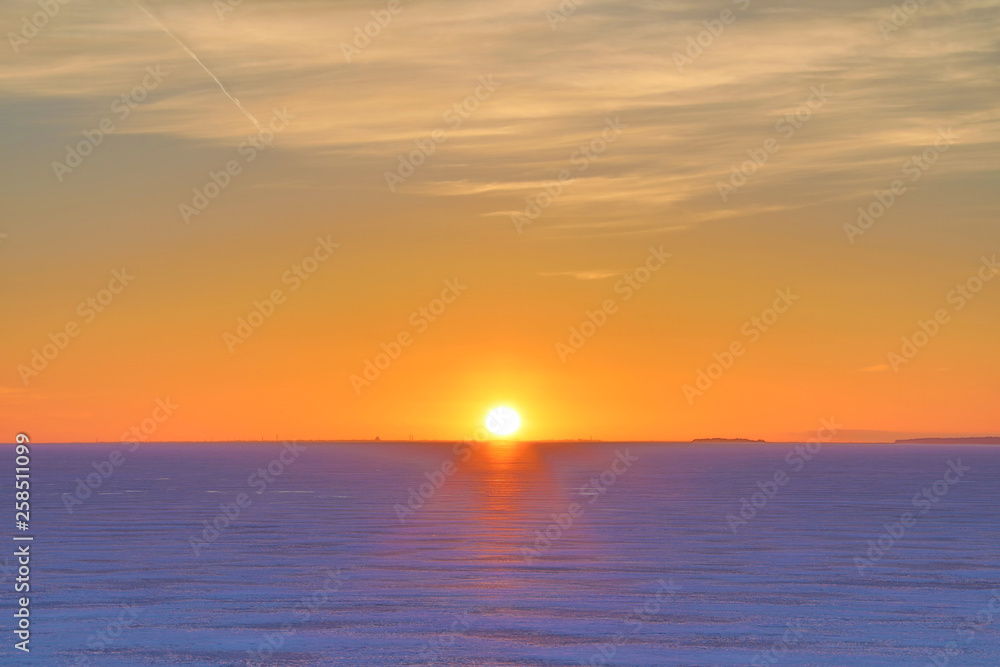 The sunset or sunrise. The cloudy sky cloured in red, orange, crimson, purple, violet and blue bright and vivid coloures with setting or rising sun over the sea, lake or bay covered with ice and snow The sunset or sunrise. The cloudy sky cloured in red, orange, crimson, purple, violet and blue bright and vivid coloures with setting or rising sun over the sea, lake or bay covered with ice and snow