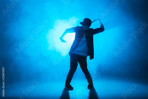Full length silhouette of a young man dancer dancing funky hip hop on isolated studio neon blue background